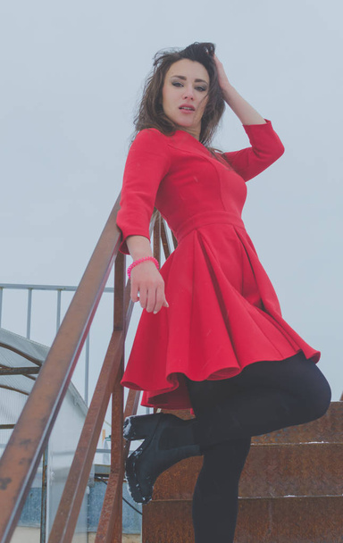 on a cloudy day girl on rusty metal staircase in a red dress - Foto, imagen