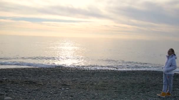 Mujer rubia con el pelo largo camina en chaqueta blanca cerca del mar el mar
 - Imágenes, Vídeo