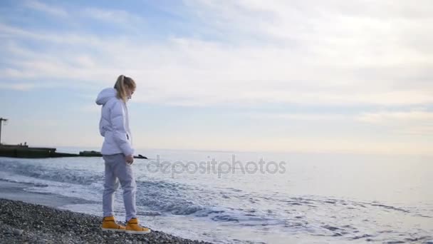 Krásná blondýnka s dlouhými vlasy chodí k moři při západu slunce - Záběry, video
