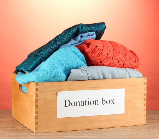 Donation box with clothing on red background close-up - Fotografie, Obrázek