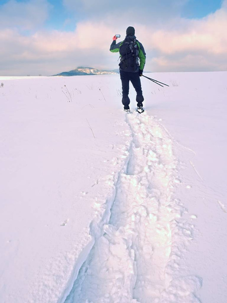 Człowiek z rakiety śnieżne i plecak robić zdjęcia za pomocą smartfonów. Turysta w zaspie - Zdjęcie, obraz