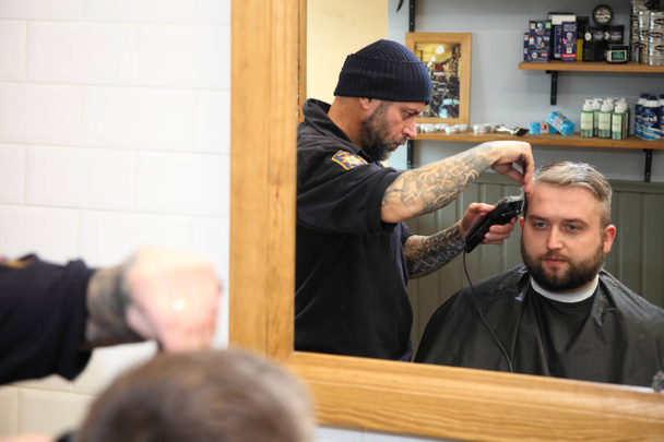 Barber coupe les cheveux du client avec une tondeuse au salon de coiffure
. - Photo, image