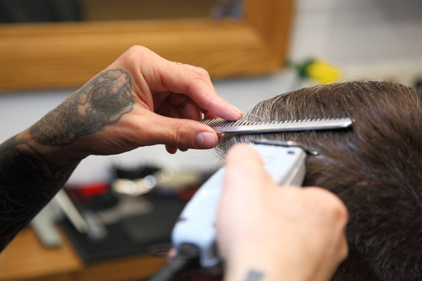 Kapper knipt het haar van de klant met clipper bij barbershop. - Foto, afbeelding