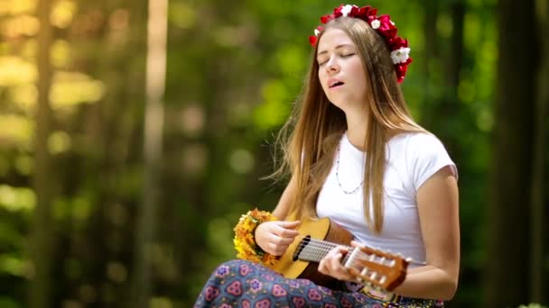 Romantická dívka v věnec z divoce rostoucích květin, cestuje se svou kytarou. Léto. - Záběry, video