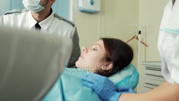 Lekarz i asystent w pobliżu pacjenta leżącego na leżaku w stomatologii - Materiał filmowy, wideo