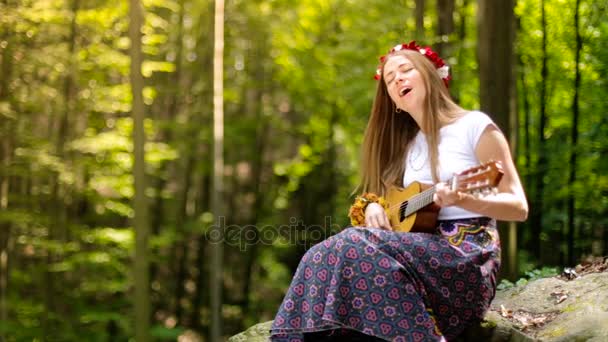 Ρομαντικό κορίτσι σε ένα στεφάνι από αγριολούλουδα που ταξιδεύουν με την κιθάρα της. Το καλοκαίρι. - Πλάνα, βίντεο