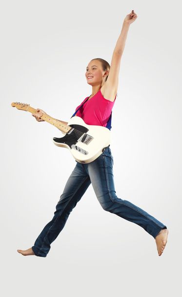 Young woman playing on electro guitar and jumping - Foto, afbeelding