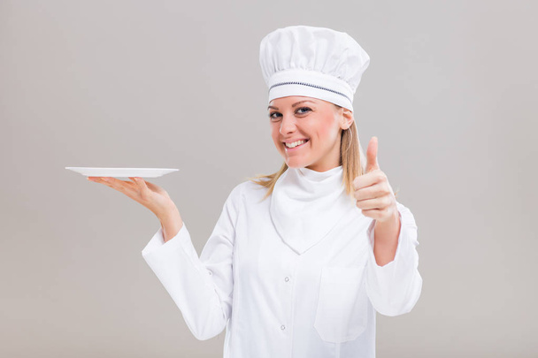 Female chef holding plate and showing thumb up - Fotografie, Obrázek
