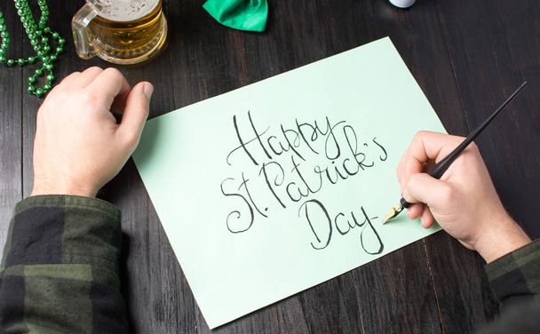 Mains masculines écrivant une carte de jour Happy St Patrick
 - Photo, image