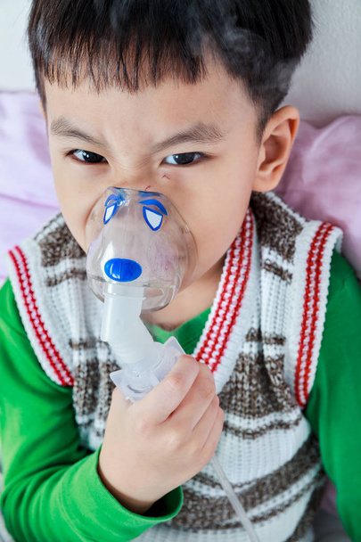 Primo piano di bambino asiatico arrabbiato tiene un inalatore di vapore maschera per il trattamento dell'asma
 - Foto, immagini