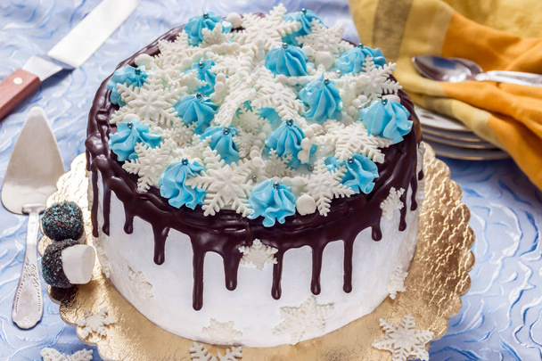 Mooie crème taart gedecoreerd met chocolade lekken, room en suiker sneeuwvlokken van mastiek, op de achtergrond van de platen, theelepels en pallet mes - Foto, afbeelding