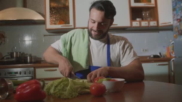 een man in de keuken kookt hij snijdt groenten - Video