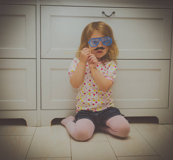 girl playing in the masquerade, tries on glasses and a mustache - Fotó, kép