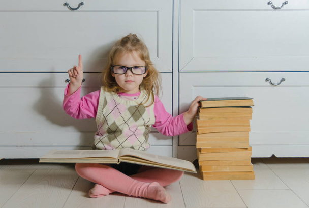  reads a book near the pile of old books kid girl with glasses - 写真・画像