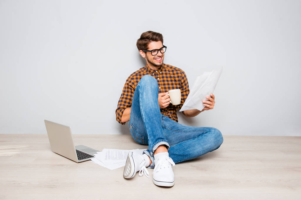 Handsome man in glasses sitting on floor and reading contract - Photo, Image