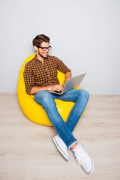 Happy smiling blogger sitting in armchair and typing on laptop - Zdjęcie, obraz