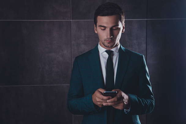 Young concentrated businessman chatting on smartphone on gray ba - Foto, immagini