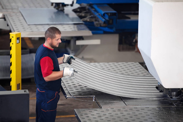 in einer Fabrik, Industriearbeiter in Aktion auf einer Metallpresse, die ein Stück Stahl zur Bearbeitung bereit hält. - Foto, Bild