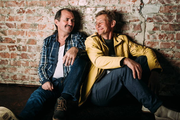 Two handsome middle aged men, dressed in casual clothing , old friends. Red brick wall background. - Fotografie, Obrázek