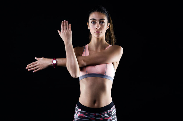 Fit and sporty young woman stretching on black background. - Photo, Image