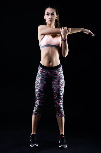 Fit and sporty young woman stretching on black background. - 写真・画像