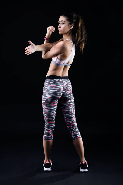Fit and sporty young woman stretching on black background. - Fotó, kép
