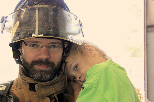 Fechar-se de um bombeiro segurando uma menina
 - Foto, Imagem