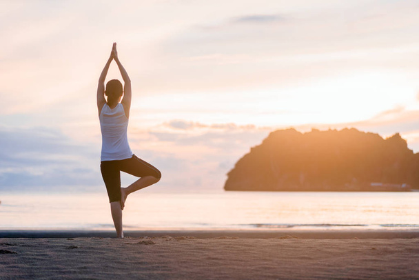 junge Frau praktiziert Yoga am Strand bei Sonnenuntergang. - Foto, Bild