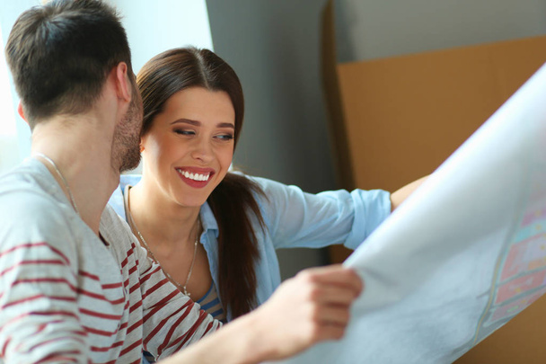 Young couple sitting on the floor and looking at the blueprint of new home - Foto, Bild
