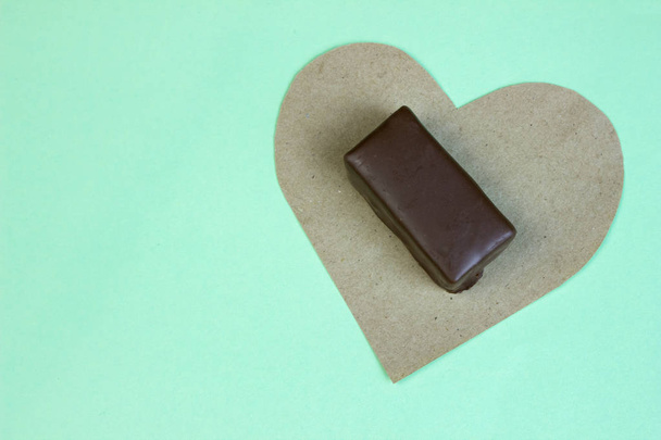 Конфетка на клочке бумажного сердца с чашкой кофе на бирюзовом фоне
 - Фото, изображение