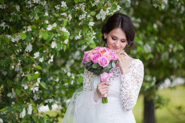 Young beautiful woman, bride with wedding bouquet in blooming garden - Photo, image