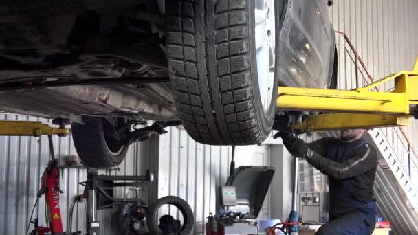 Male mechanic repairing underneath lifted car at garage - Footage, Video