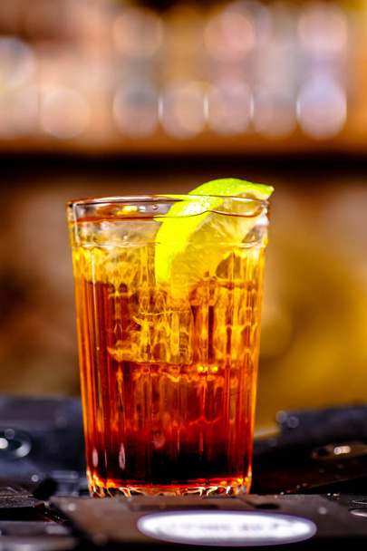 Cocktail marrone con una fetta di limone versata in un bicchiere sfaccettato
 - Foto, immagini