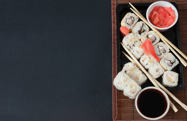 Varios tipos de rollos de sushi servidos sobre fondo negro. Concepto de comida para llevar Sushi
 - Foto, imagen