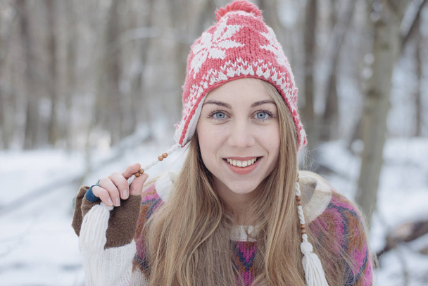 Téli portré fiatal gyönyörű szőke nő, fárasztó kötött sapka. Hó a téli szépségápolási divat fogalmát. Havas erdei háttér. - Fotó, kép