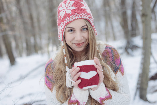 Talvinen nainen pitelee mukia lämmittääkseen. Söpö nuori nainen juo teetä tai kahvia ulkona
 - Valokuva, kuva