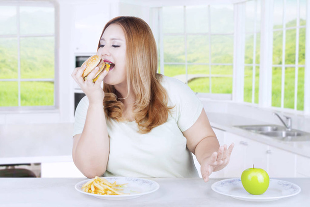 Mujer rubia comiendo hamburguesa en la cocina
 - Foto, Imagen