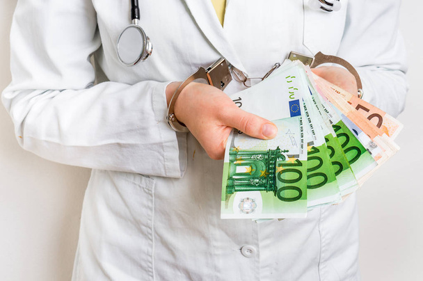 Médico con dinero en euros y esposas - concepto de soborno
 - Foto, Imagen
