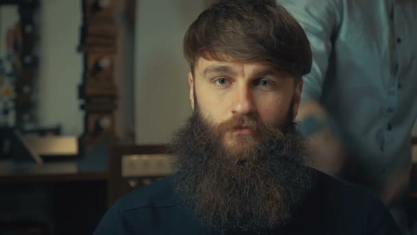Jonge knappe kapper maken kapsel van aantrekkelijke bebaarde man in kapperszaak - Video