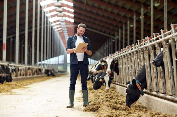 farmer with clipboard and cows in cowshed on farm - Fotografie, Obrázek