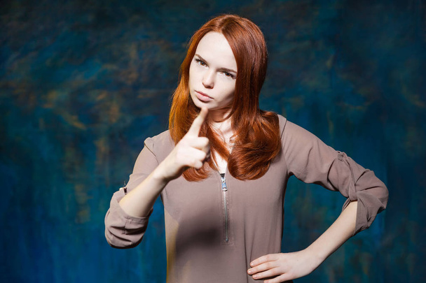 Strict red haired girl shows finger with arms akimbo - Фото, изображение