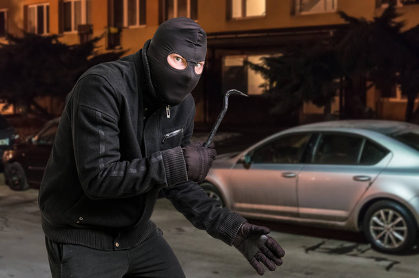 Masked thief in balaclava with crowbar wants to rob a car - Photo, Image