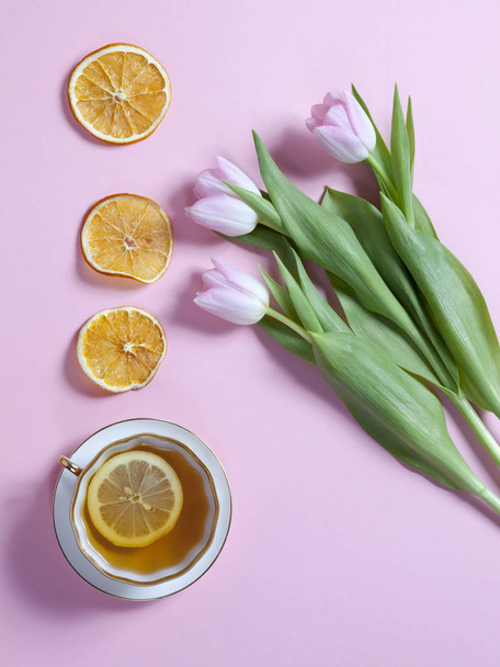 Cup of tea with lemon, Pink tulips flowers arrangement with dry orange slice on pink background. Copyspace - Фото, зображення