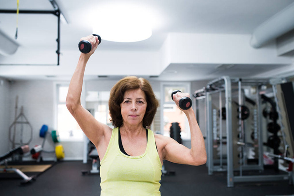 Senior woman in gym working out with weights. - Zdjęcie, obraz