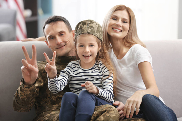 Soldier in camouflage and his family sitting on sofa at home - Foto, Bild