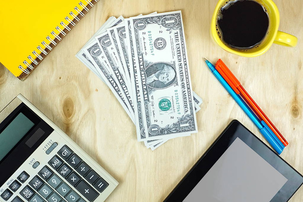Amerikai dollár-bankjegyek és pénzügyi számológép, tablet Pc és a csésze kávé a fából készült asztal. - Fotó, kép