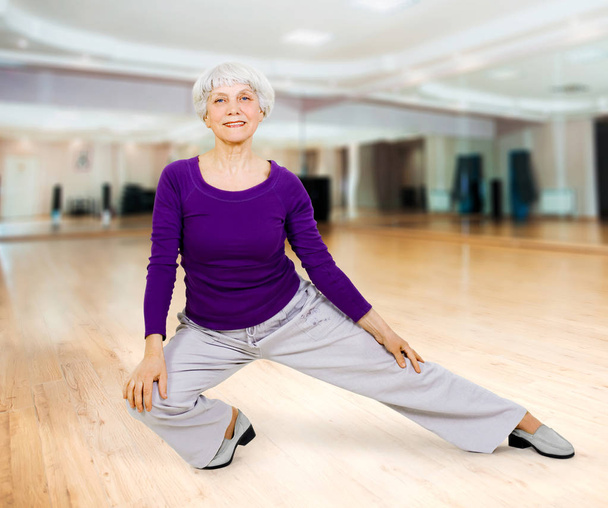charming beautiful elderly woman doing exercises while working out playing sports in fitness training room - Photo, Image