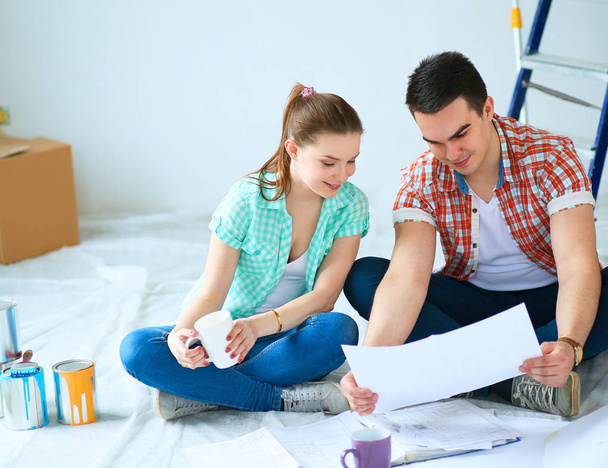Young couple sitting on floor with apartment plan - Foto, Imagen