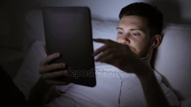 man with tablet pc and earphones in bed at night - Materiaali, video