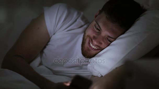 young man with smartphone in bed at night - Séquence, vidéo